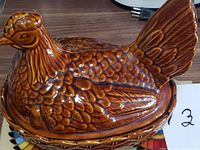 Side view of brown glazed ceramic hen on nest covered dish