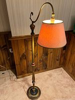 Floor lamp standing lit showing the design, warm lampshade light, metal and wood elements, and curved arm with shade.