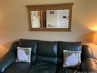 Wall mirror hung above a dark green sofa with floral pillows to show size and placement in room