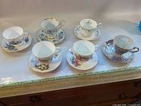 Full set of six assorted porcelain/bone china tea cups and matching saucers displayed on wooden surface with ruler for scale