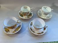 Four assorted vintage bone china tea cups with matching saucers, featuring different floral patterns and gold trim, arranged on a flat surface under natural light.