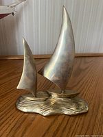Brass sailboat sculpture showing two sailboats with large sails on a textured base mimicking waves.