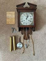 Full clock with key, pendulum, weights and instruction sheet laid out showing all components and clock front.