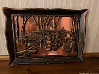 Full view of framed copper relief wall art showing outdoor pioneer homestead scene with trees, kettle, and figures in rustic setting.