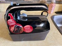 Front and side view of black Hamilton Beach hand mixer with pulse function sticker and attached storage case.