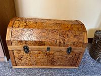 Front and top view of wooden chest showing floral and nature hand-carved motifs and metal latch hardware.