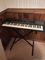 Digital keyboard and stand set against a wood-paneled wall, showing full keyboard and stand setup.