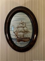 Frontal image of large oval frame showing ship artwork, glossy dark wood grain finish with curved border
