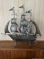 Front view of the metal ship sculpture showing the detailed sails, flags, and stand.