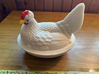 Full view of the milk glass hen-shaped lid piece on the nest base showing red comb and yellow beak accents, texture details of feathers and basket weave base.