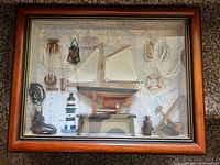 Front view of shadow box showing entire collection of nautical-themed miniatures inside a wooden frame with glass front. Background is a map.