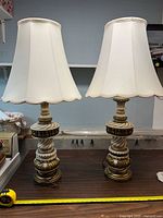 Pair of ceramic lamps with shades on, showing ivory and gold designs, approximately 38 inches tall