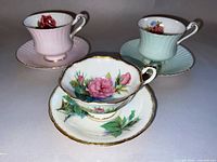 Three Paragon fine bone china teacups and saucers with floral designs and gold trim shown from a front angle on a white surface.