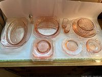 Full view of all 23 pink depression glassware items arranged on white paper, showing two platters, dishes, bowls, and shaker