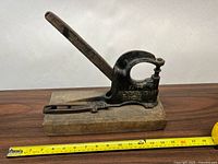 Side view of the antique cast iron and wood notary seal press with wooden base and measuring tape for scale.