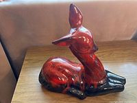 Side view of the red and black glazed ceramic deer figurine sculpture showing shape and color detail.