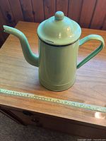 Photo showing the side view of the pale green enamel metal coffee pot with lid, handle, and spout on wooden surface with measuring tape showing approximately 8-9 inches height.