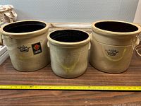 Photo showing all three vintage Crown stoneware pickling crocks arranged side by side on a wooden surface with a measuring tape in front for size reference.