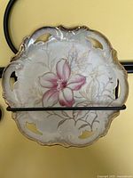 Top/front view of the lustreware plate showing the pink flower, gold foliage design, ornate cutwork handles, and scalloped pierced edges with an iridescent finish.