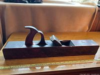 Side view of vintage wooden hand plane joiner showing curved wooden handle and body with metal blade slot