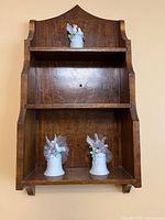 Brown wooden wall-mounted display shelf with 3 porcelain bird and flower figurines, shown from front