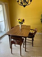 Side view of the wooden dining table with three chairs visible, showing the tapered legs and table surface.