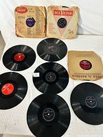 Seven 78 RPM vinyl records laid out with visible labels and vintage sleeves including RCA Victor and Decca Records.