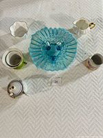 Overview of antique milk glass bowls, cups, creamer, sugar bowl, and decorative blue glass bowl on white cloth surface