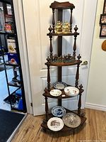 Full view of antique five-tier chestnut wood whatnot shelf with all items displayed: brass bookends, coachmen bookends, and commemorative plates.