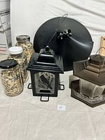 Photo showing two bird feeders, a round black squirrel baffle, and three jars of bird seed on a light-colored surface.