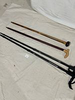 Four items laid out on fabric: two wooden canes and two black hiking poles with adjustable segments and wrist straps.