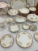 Complete hand-painted Empress China set arranged for display. Stack of plates, several bowls, cups, saucers, serving dishes, cream and sugar bowl all visible with intricate floral designs and bordered edges.
