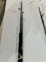 Photo showing two black fishing rods placed on a white textured surface, rubber-banded for protection and grouping.