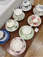Top view of 7 teacup and saucer sets on a wooden table showing various floral patterns and delicate handles