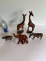Photo showing all five African animal carvings with water bottle for scale: two wooden giraffes, wooden elephant, wooden zebra, and small stone hippopotamus.