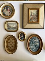 Collection of six miniature framed paintings with varied subjects and frames arranged on white surface