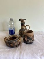 Full set of three handmade pottery items shown with a water bottle for scale: a pitcher, a small container with two handles, and a vase/container. All painted with black stylized pomegranates on natural clay.