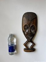 Full view of the carved African mask next to a standard water bottle for size reference, showing overall shape and dimensions.