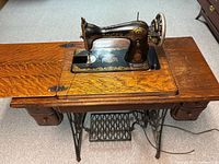 Full view of the Singer sewing machine set into wooden cabinet with fold-out table extension and two storage drawers.