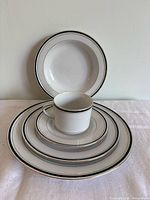 Photo showing stack of dinner plates, salad plates, soup plates, and one cup stacked on a saucer, displaying the set design and rim details