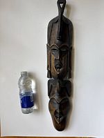 Photo of full mask with water bottle for size reference, showing two vertical faces and the two-tone wood color.