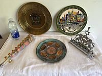 Photo showing all five items on white cloth: three plates, two menorahs, and a water bottle for scale.