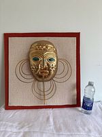 Front view of the mounted metal replica mask with water bottle next to it for size reference