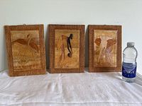 Three African wooden framed pictures displayed upright with a water bottle for size reference.
