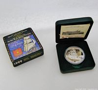 Coin and original presentation box side by side showing commemorative text and artwork on the box.