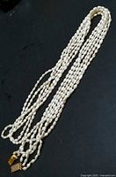 Full view of three strands of white freshwater pearl necklace with gold clasp laid out against black background.