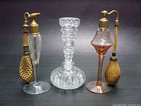Front view of two etched glass and brass perfume atomizers and one cut glass bottle with stopper, displayed together