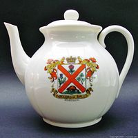 Front view of white porcelain teapot displaying Montreal Coat of Arms with red saltire, floral symbols, beaver and 'Concordia Salus' motto.