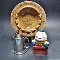 Photo showing all three Humpty Dumpty themed items: brown pottery ashtray, pewter child's mug, and colorful salt & pepper shakers.