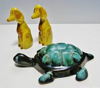 Two small long-eared dog figurines in harvest gold glaze standing, alongside one blue-green glazed turtle figurine lying flat.